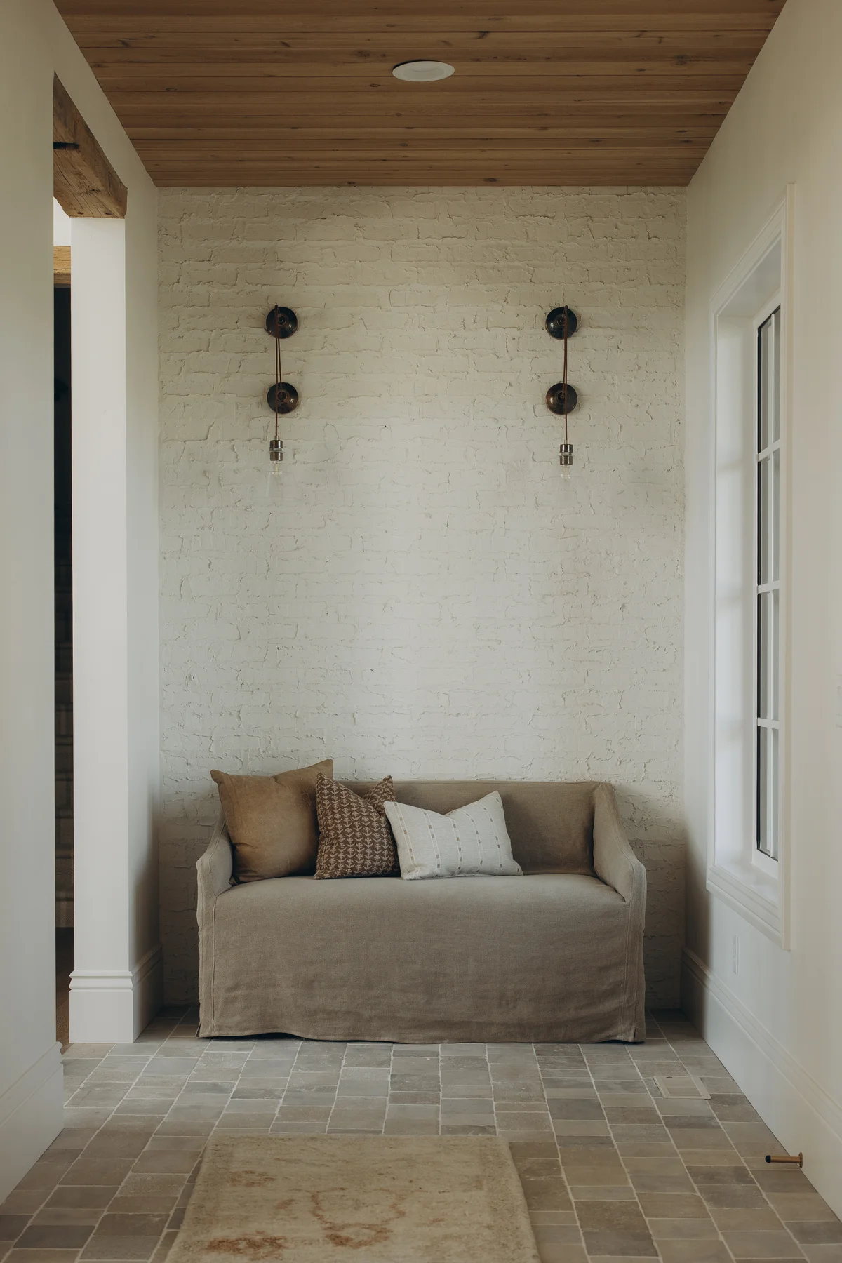 Painted-brick hallway nook with linen settee and cobblestone tile floor